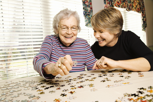 Elderly woman and a younger woman work on a jigsaw puzzle.