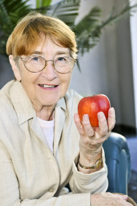 Senior woman with glasses holding apple and smiling