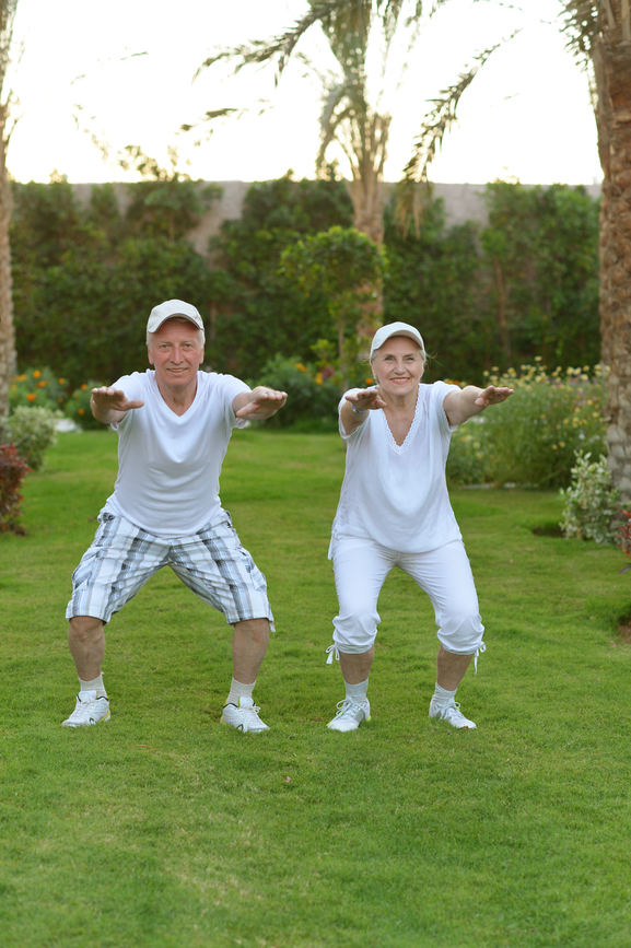 2 seniors exercising on the grass near palm trees