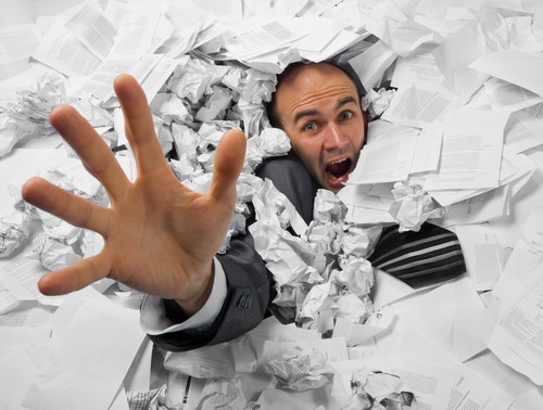 Man sinking in heap of documents and asking for help
