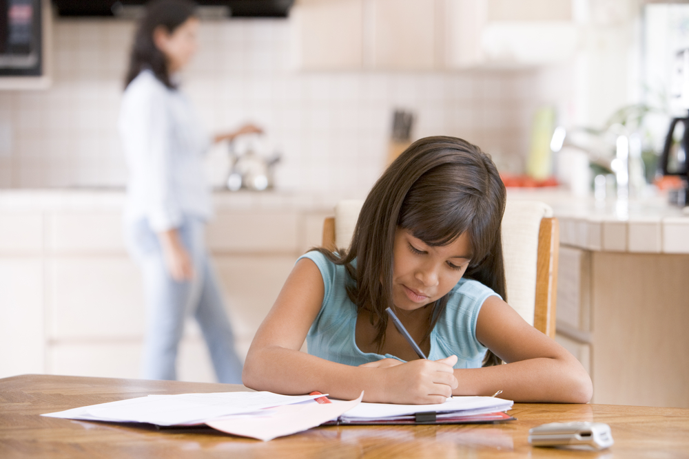 Young girl in kitchen doing homework with woman in background