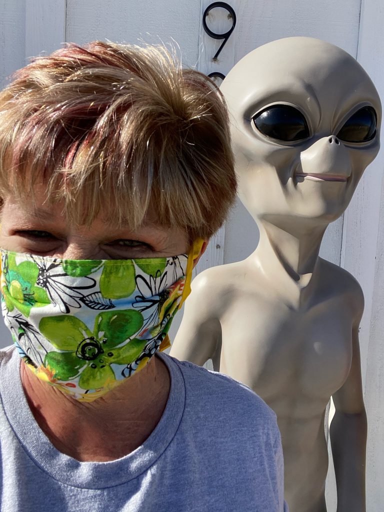 Shelley, wearing a COVId mask and standing next to an ET outside The Wine and Rock Shop in Yucca Valley