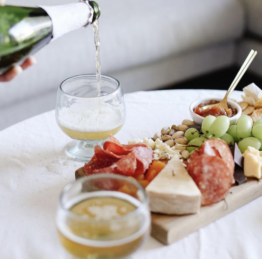 charcuterie board on a white table. Someone is pouring a glass of champagne.