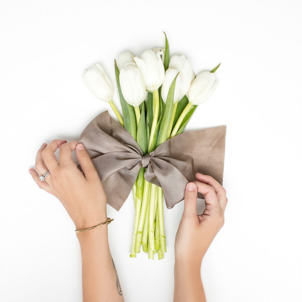 a gift of lillies wrapped in burlap showing tow hands tying a bow around them