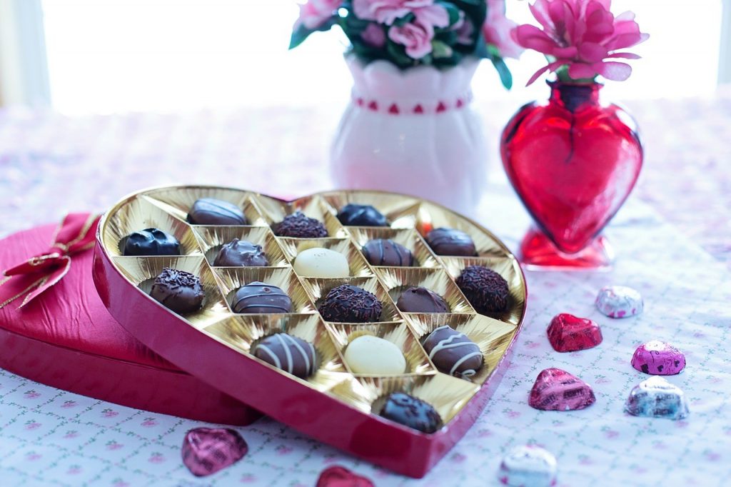 a heart shaped box with candy in it and flowers to the side 