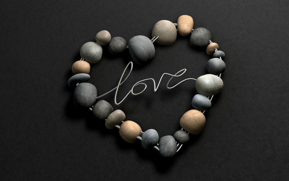 A handcrafted heart shape made out of wire and stones with the word Love spelt out on a stone background