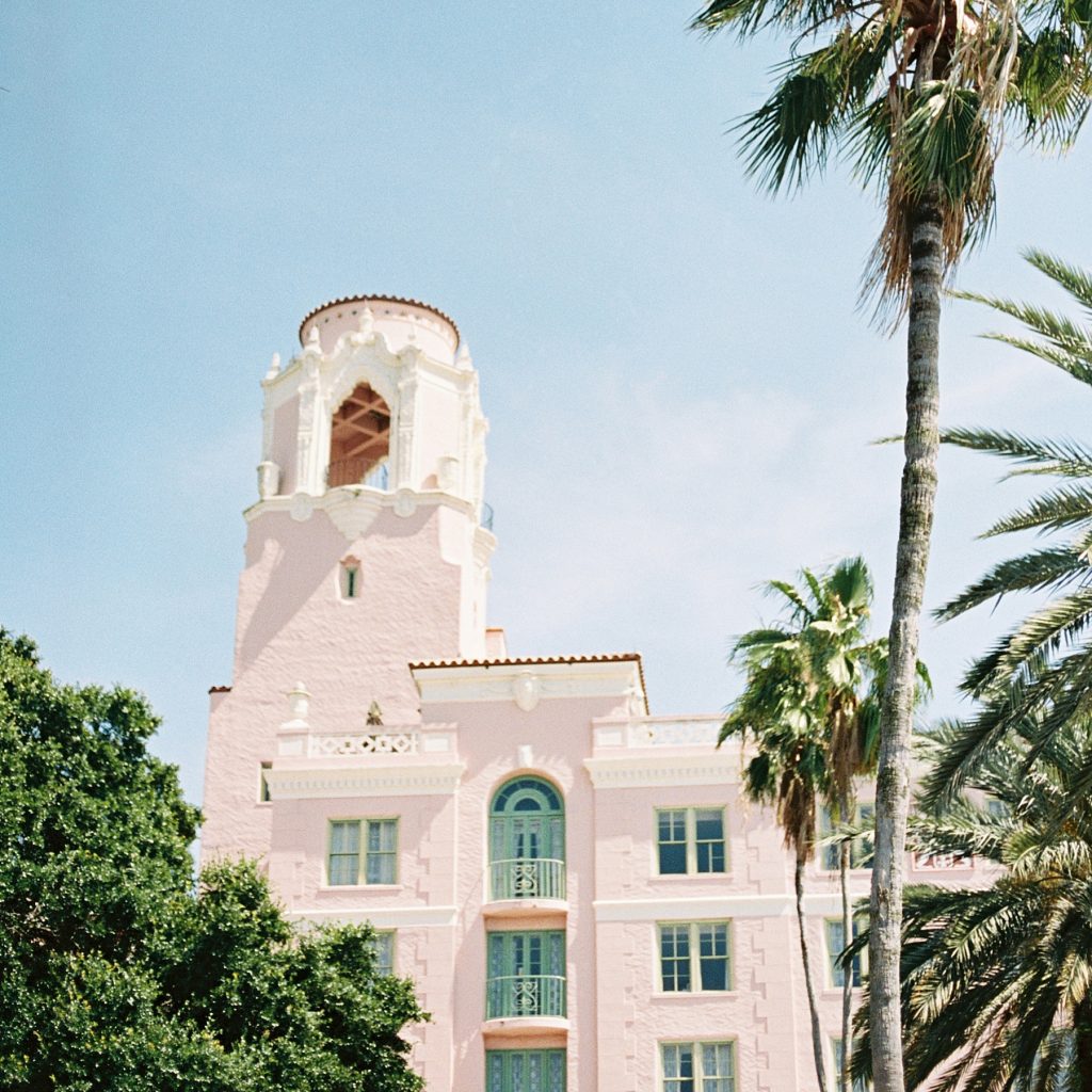 a creamy white mission-shaped building with a palm tree beside it