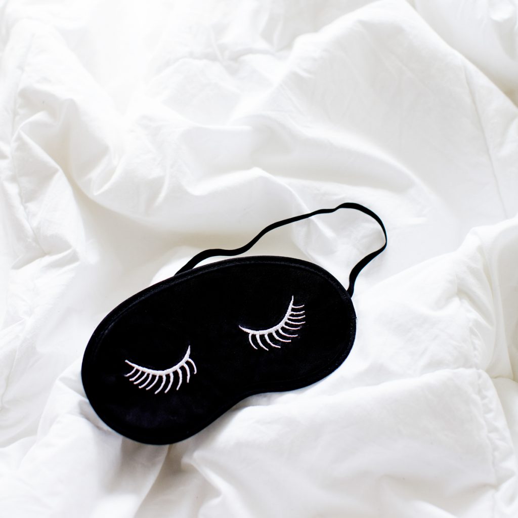 a sleep mask with eyelashes on it lying on messy bedcovers