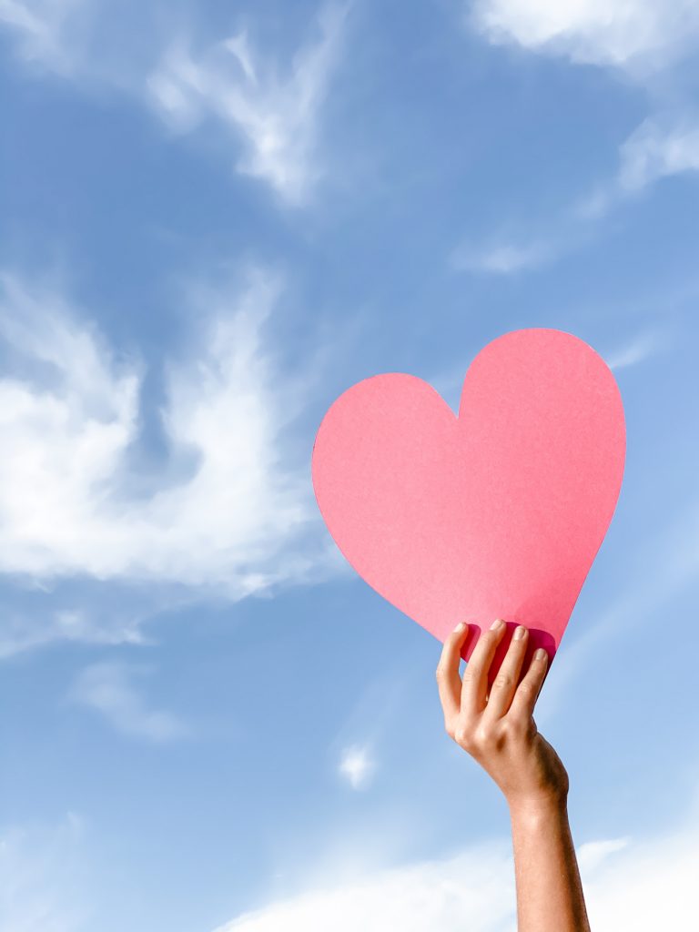 hand holding a pink paper heart into the sky