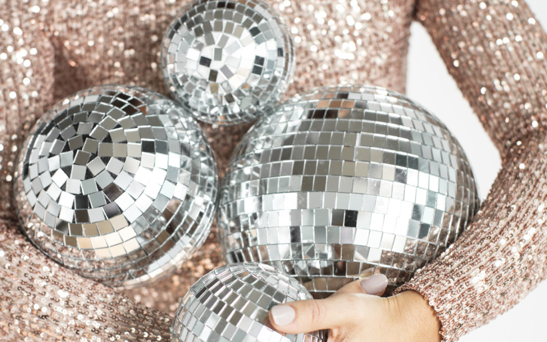 close up of a woman wearing a glittery dress holding different sizes of silver glitter balls