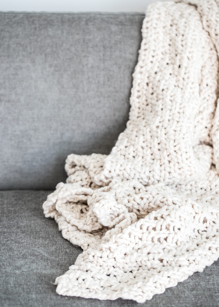 a Cozy cream-colored afghan draped over a grea armchair