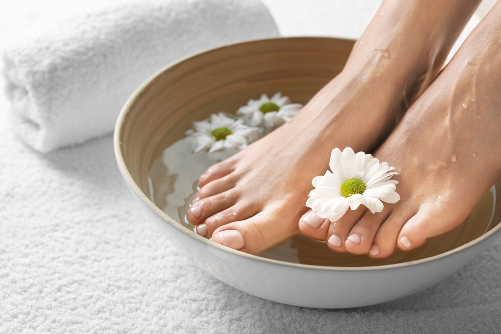 a woman's feet in a tub of foot soak and daisies