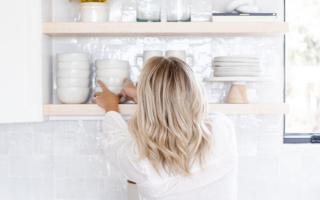 a woman standing in front of her kitchen shelves, facing a way from the camera