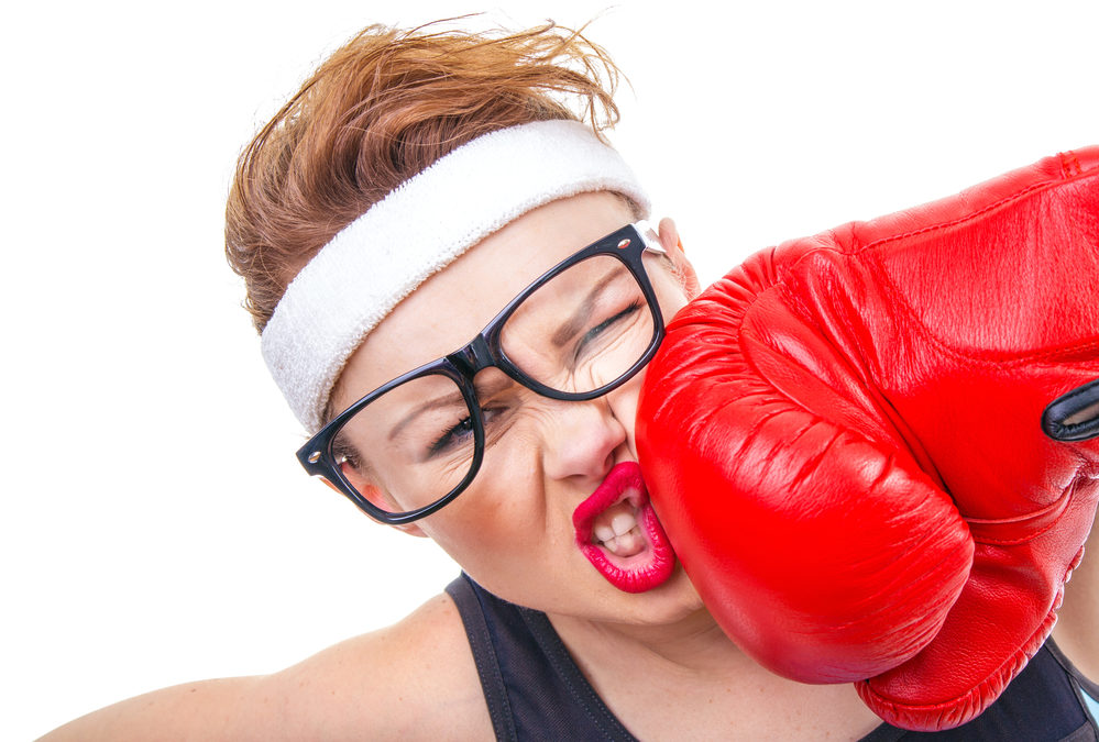 woman appears to be punched by a large red glove. She is wearing a white sweat band Her glasses are askew.