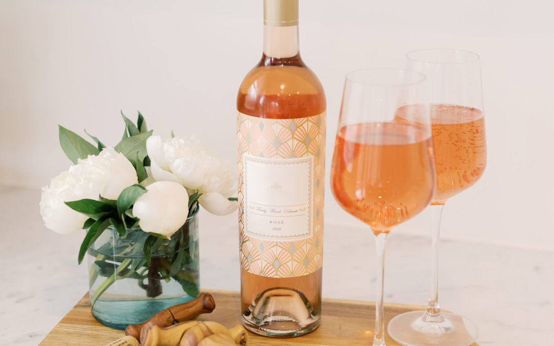 a bottleof rose with 2 glasses beside it sitting on a cheese board. There is a bouquet of flowers in a vase to the left of the wine bottle,