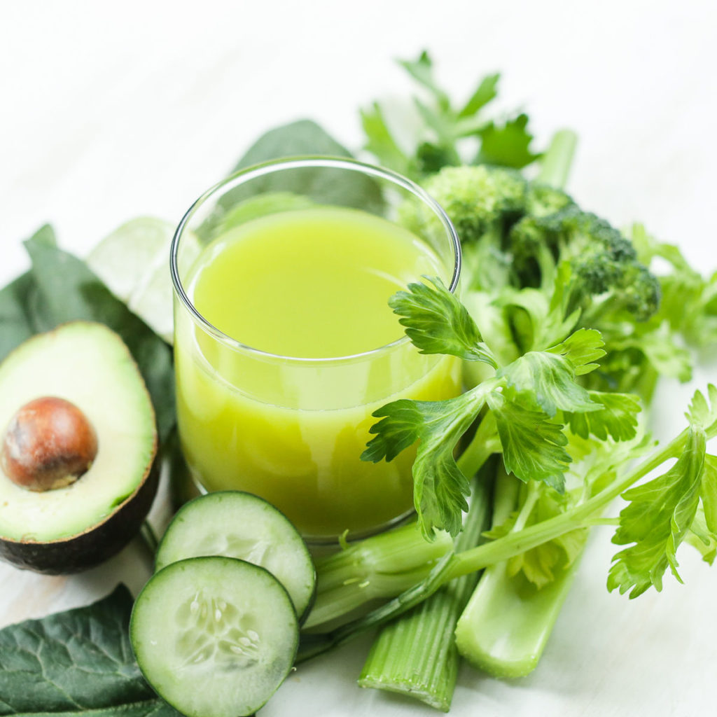 A glass of celery juice surrounded by celery stalk, avocado and cucumber slices